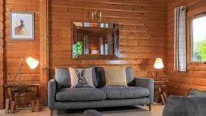 A cozy cabin interior with a grey sofa, two side tables with lamps, a mirror, and a framed picture on the wall.
