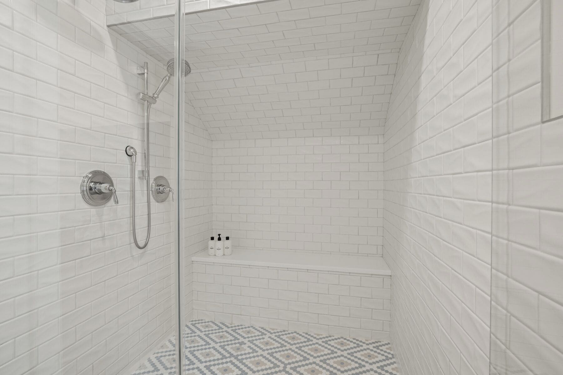 A shower with white tiled walls and a patterned floor.