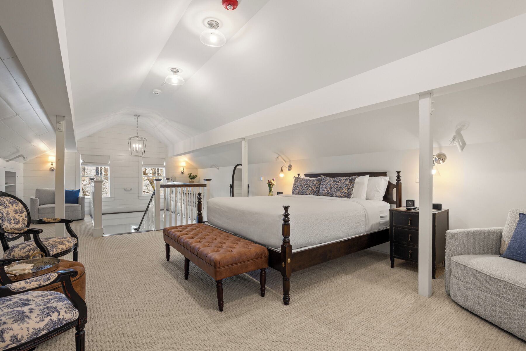 A spacious bedroom with a large bed, a nightstand, a bench, and a chair.