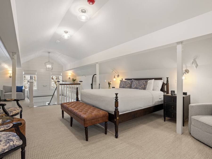 A spacious bedroom with a large bed, a nightstand, a bench, and a chair.