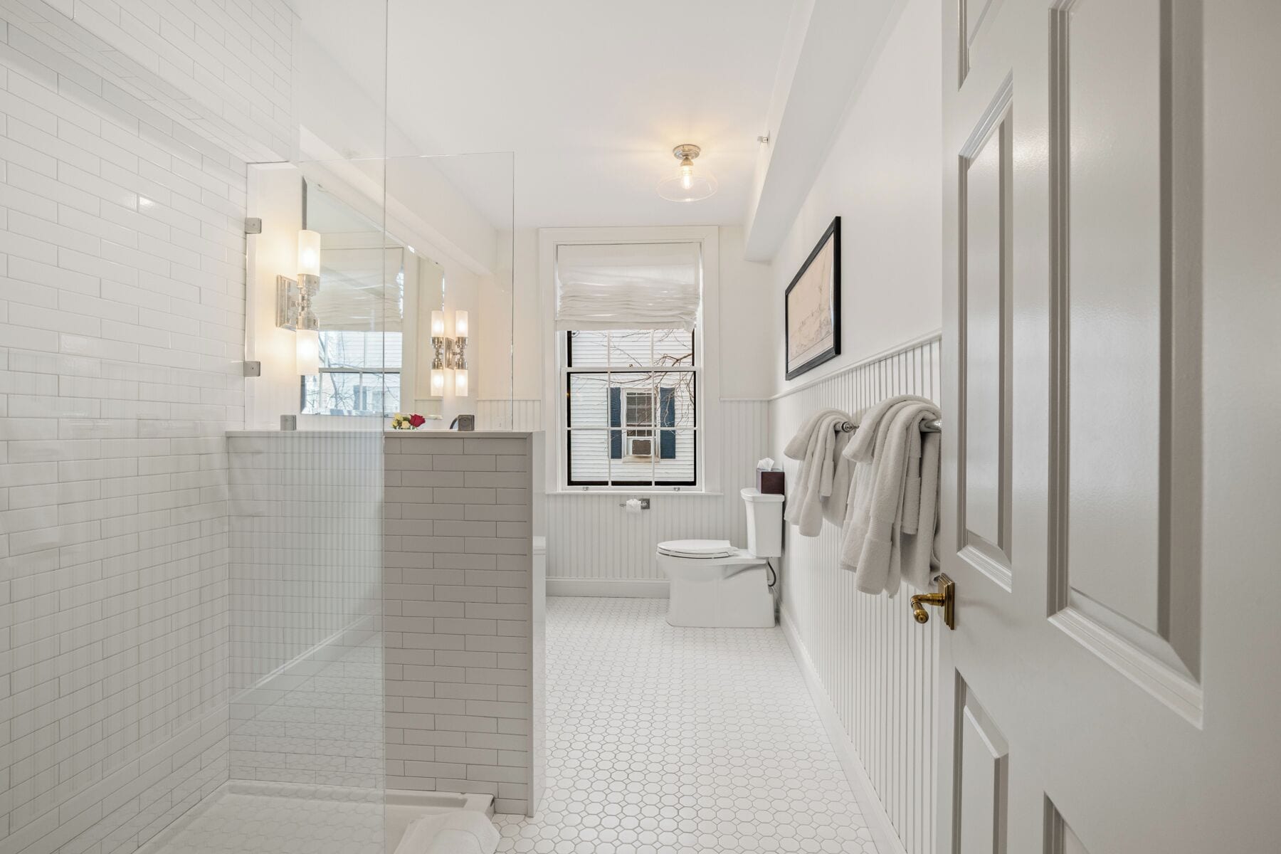 A modern bathroom with white tiled walls, a hexagonal floor pattern, a glass shower enclosure, a toilet, and a towel rack.