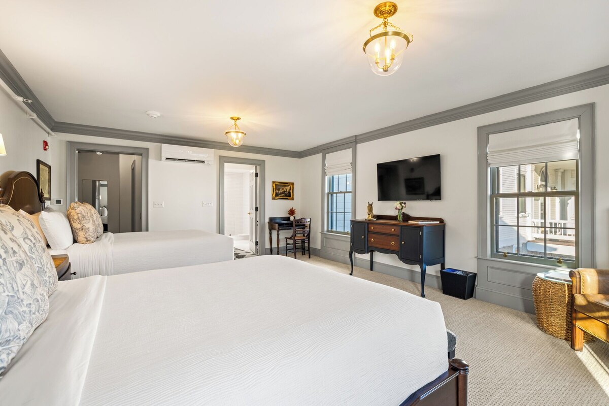 A hotel room with two beds, a desk, a chair, a television, and a window.