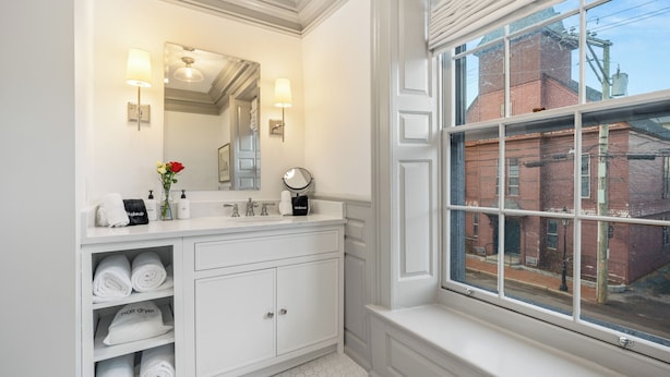 A bathroom with a large mirror, two sinks, a vanity with storage, a window with a view of buildings, and a towel rack with towels. - The Davenport Inn (Portsmouth)