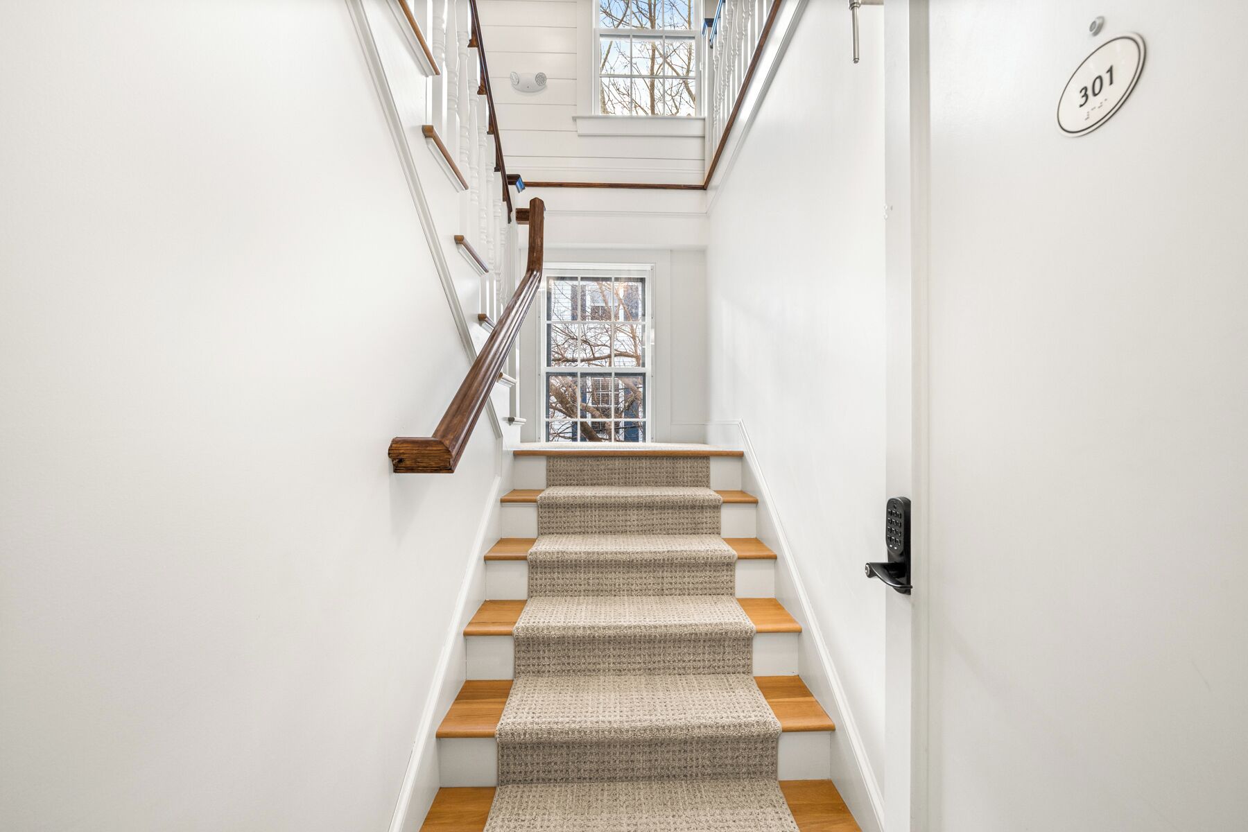 Una escalera con escalones de madera y un rellano con alfombra, que lleva a una puerta con el número 301.