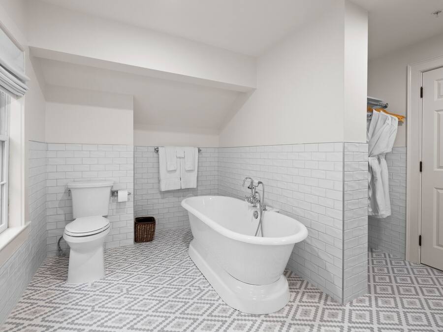 A bathroom with a white toilet, a freestanding bathtub, and a window.