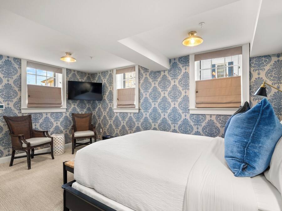 Une chambre à coucher avec un grand lit, deux fauteuils, un téléviseur et un papier peint à motifs.