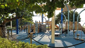 A playground with various play structures, surrounded by trees and bushes.