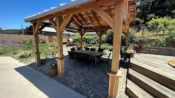 En træpergola med en stenbelagt terrasse og et bord med stole under.