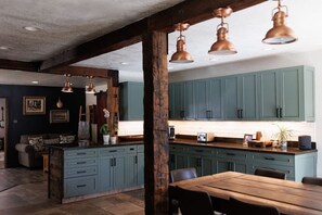 A kitchen with teal cabinets, a wooden island, and copper pendant lights.