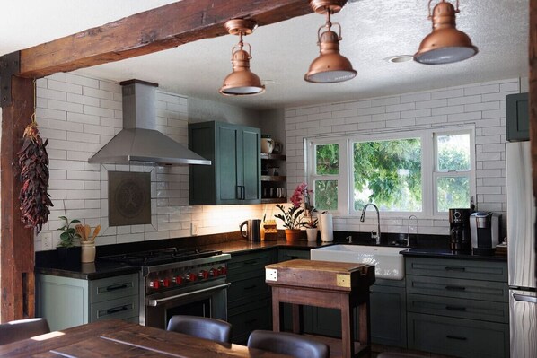 A kitchen with a stove, oven, and sink, wooden table, and hanging lights.