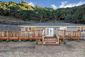 Une maison à deux étages dotée d’une terrasse en bois et d’un escalier menant à la porte d’entrée.