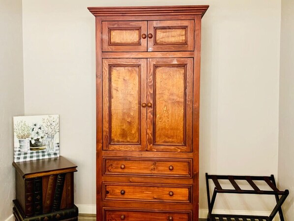 Un alto mobile in legno con diversi cassetti e ante, posto tra un tavolino con un quadro e una sedia.