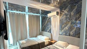 Una habitación de hotel moderna con pared de mármol, dos camas, una mesita de noche y una lámpara en el techo.