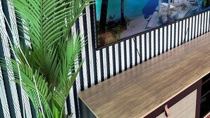 Un televisor muestra una escena de un resort tropical, un mueble bajo de madera y una planta de palma verde grande.