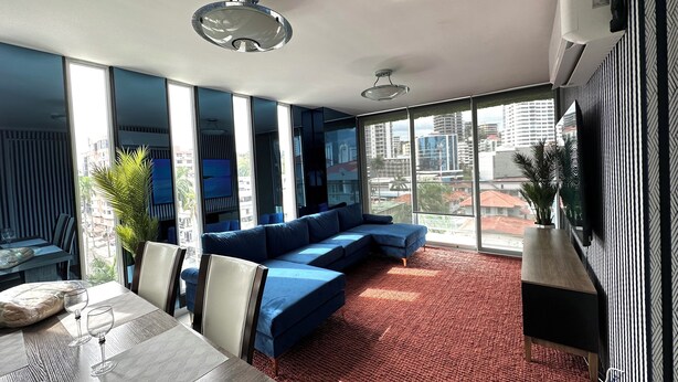 Una sala moderna con un amplio sofá modular, una mesa de comedor con sillas y un gran ventanal con vistas a la ciudad.