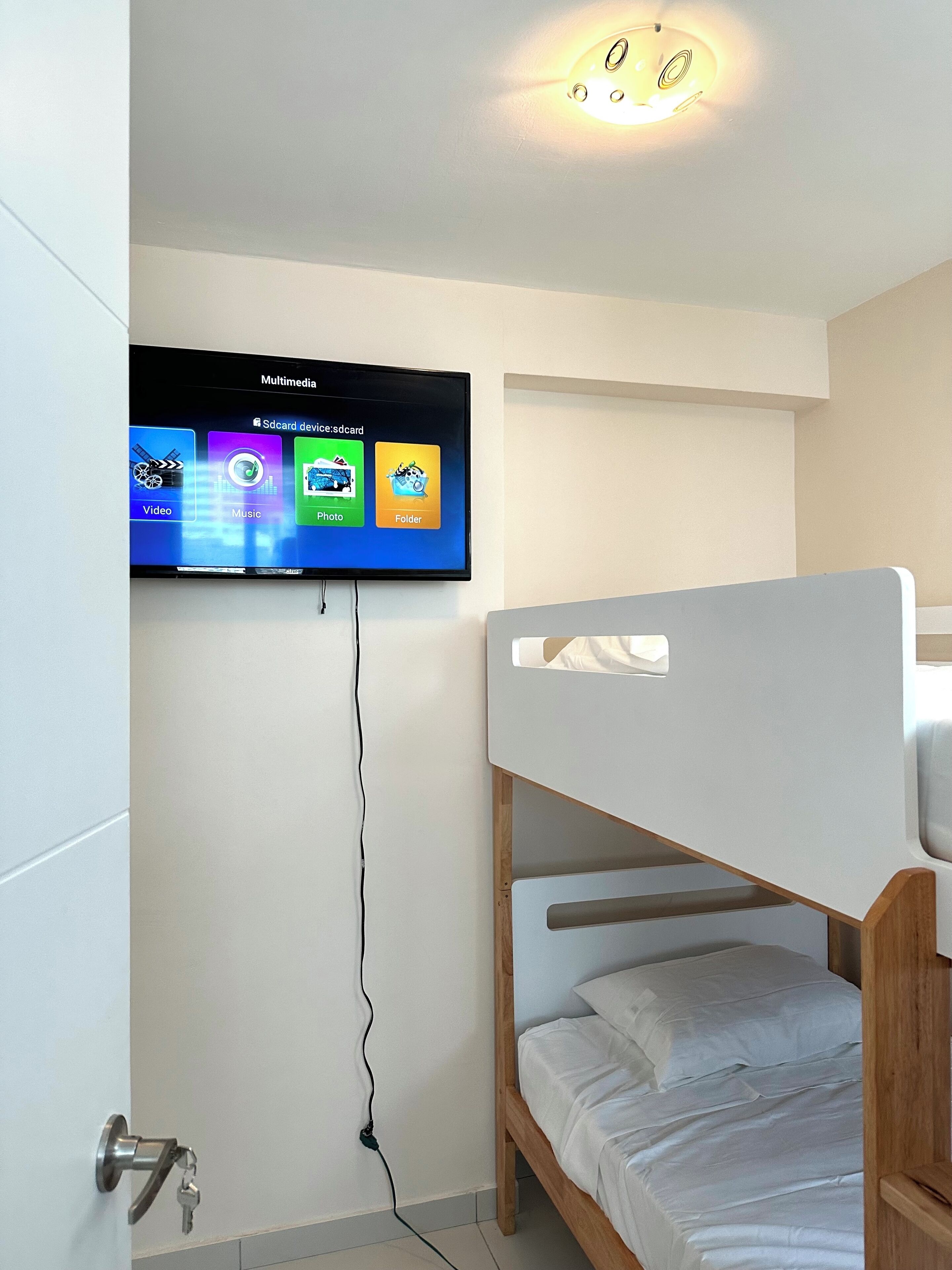 A room with a bunk bed, a television mounted on the wall displaying multimedia apps, and a visible power outlet.