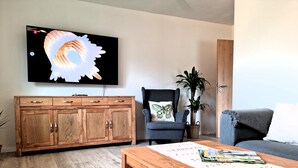 A living room with a wooden cabinet, a television, a chair with a butterfly pillow, a potted plant, and a coffee table with puzzle pieces. - Heidezauber: Modern vacation apartment with terrace and fireplace (Uelzen)