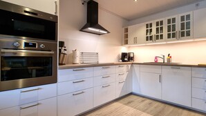 A modern kitchen with stainless steel appliances, white cabinetry, and a built-in oven. - Heidezauber: Modern vacation apartment with terrace and fireplace (Uelzen)