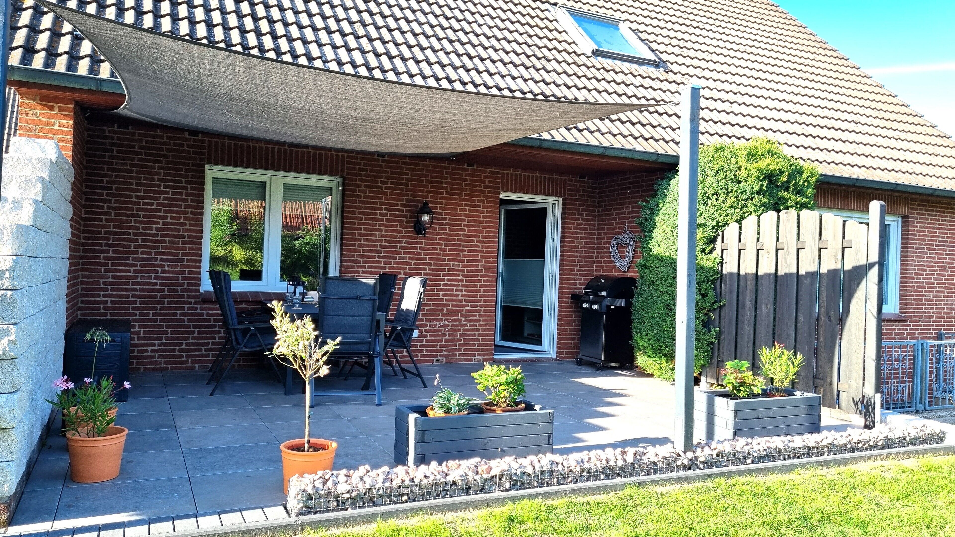 Un patio con una mesa y sillas, una casa de ladrillo, una valla de madera y plantas en macetas.