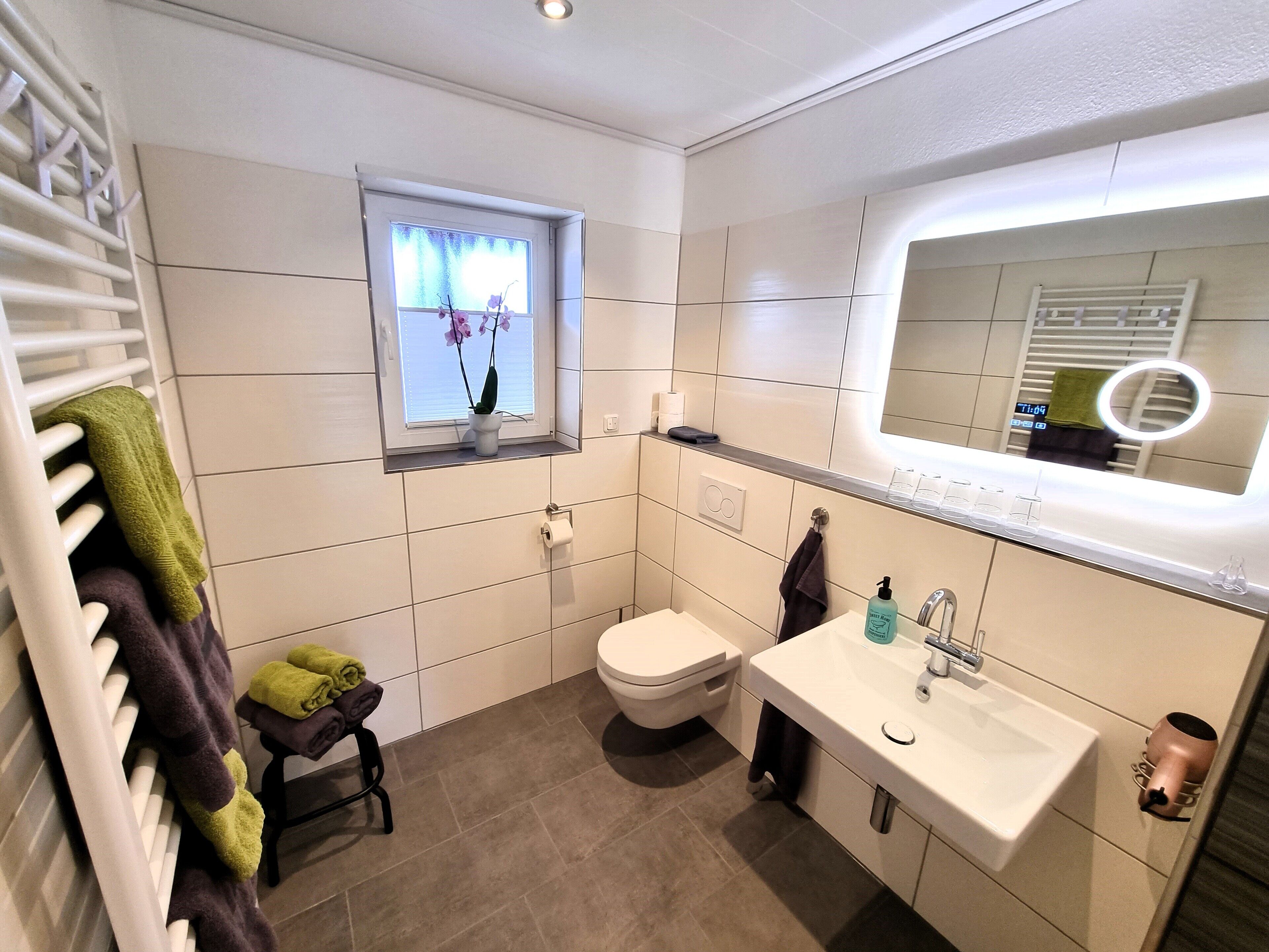 Un baño moderno con inodoro, lavamanos y ventana con una orquídea en maceta.