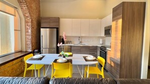 A modern kitchen with white cabinets, a stainless steel refrigerator, and a dining area with a round table and yellow chairs.