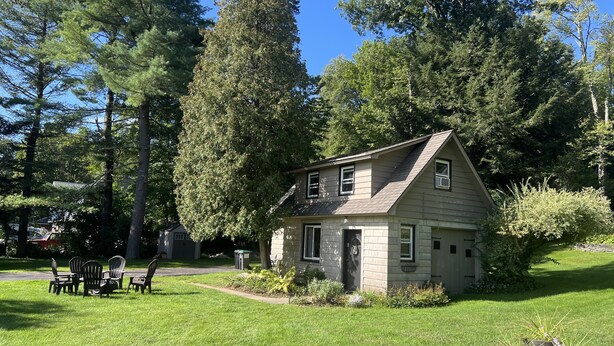 A small two-story house with a sloped roof, surrounded by a well-maintained lawn and tall trees. - Looking for a getaway? This is the perfect cottage for you.  Pet friendly! (Schenectady)