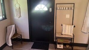 A room with a black door, a dreamcatcher, a bench with a patterned cushion, and a metal shelf with items. - Looking for a getaway? This is the perfect cottage for you.  Pet friendly! (Schenectady)