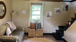 A living room with a ceiling fan, a window with curtains, a sofa, a loveseat, and a staircase. - Looking for a getaway? This is the perfect cottage for you.  Pet friendly! (Schenectady)