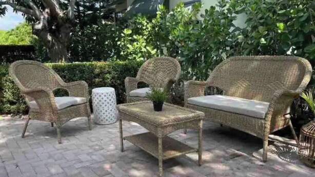 Wicker furniture with cushions and a small table, set on a paved patio with a hedge in the background.