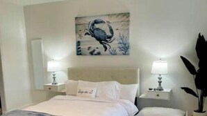 A bedroom with a bed, two bedside tables, a nightstand, a wall-mounted lamp, and a large painting.