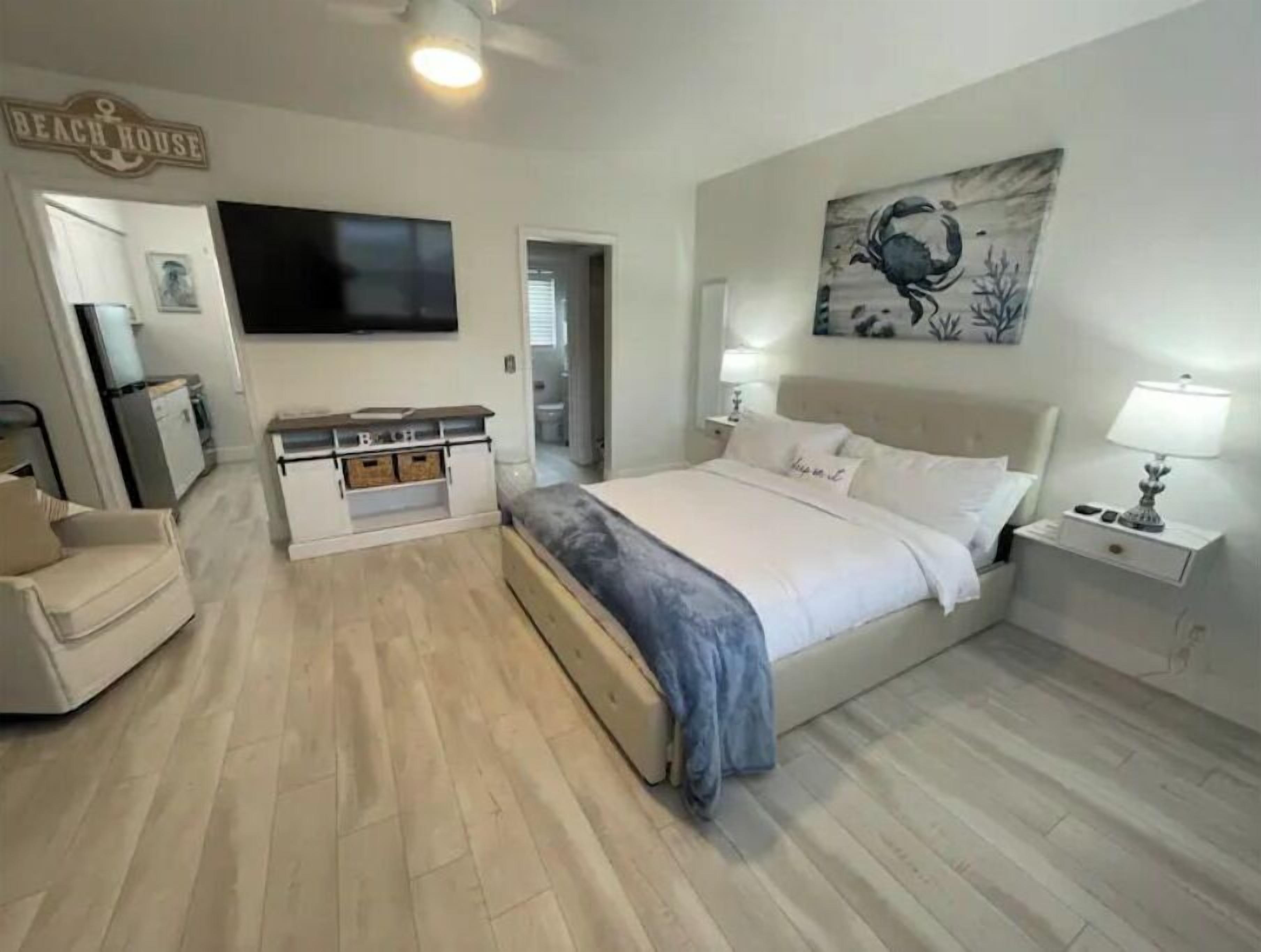 Une chambre à coucher avec un lit, des tables de chevet, une télévision, un tableau et une pancarte sur laquelle on peut lire « Maison de plage ».