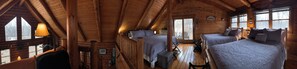 A log cabin with two beds, a wooden ceiling, and large windows.