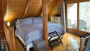 A wooden cabin bedroom with a bed, bedside table, and a view of the outdoors. - Make Memories - Secluded Log Cabin on Marion Lake Channel with Private Dock (Richville)