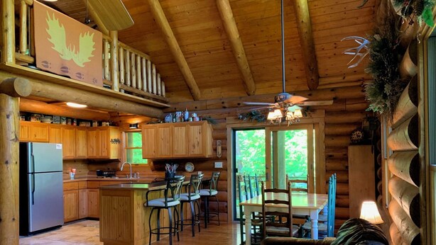 A log cabin interior with a kitchen, dining area, and a cozy seating area. - Make Memories - Secluded Log Cabin on Marion Lake Channel with Private Dock (Richville)