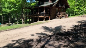 A log cabin with a porch, a deck, and a dirt driveway leading to it. - Make Memories - Secluded Log Cabin on Marion Lake Channel with Private Dock (Richville)