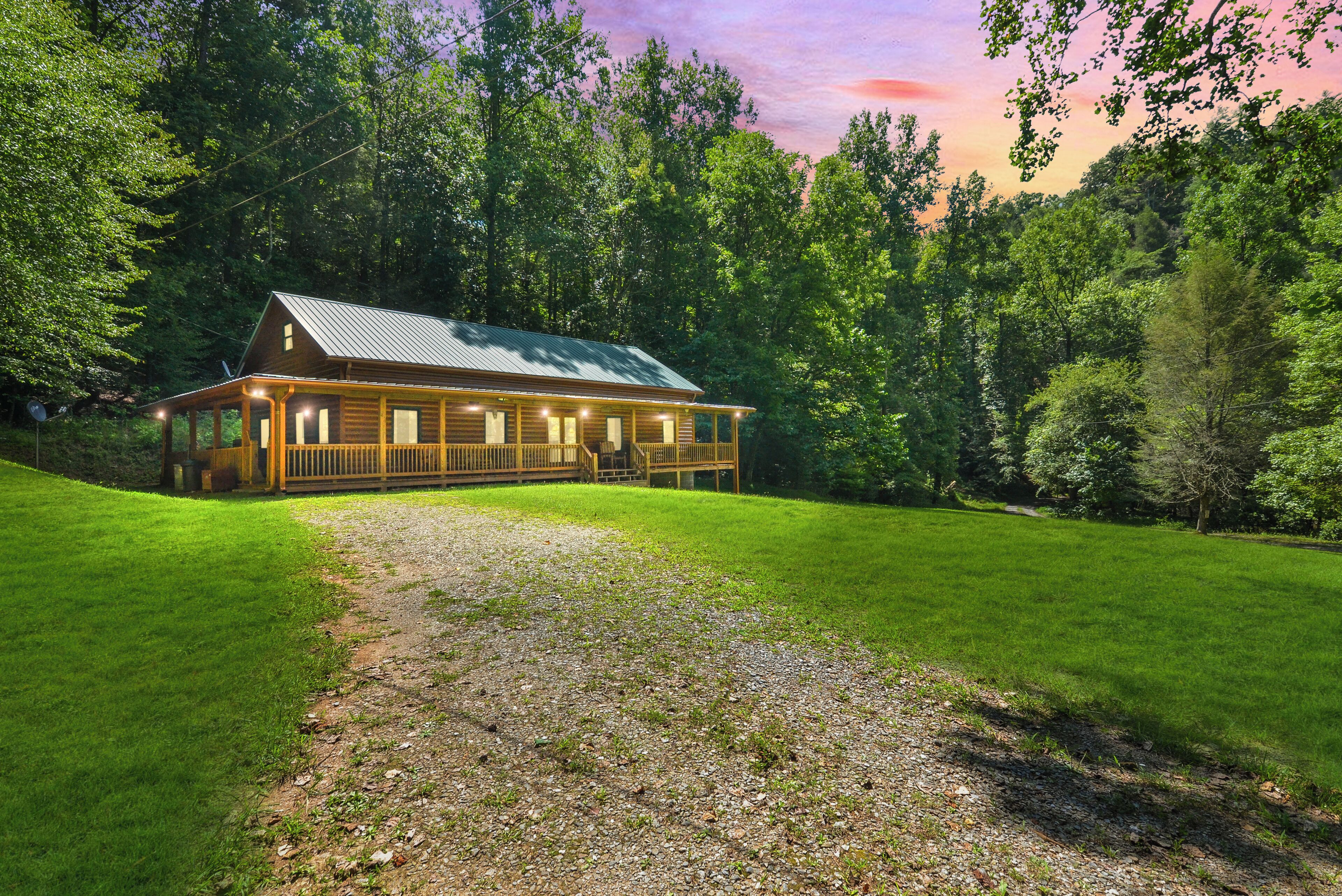 A wooden cabin with a porch, surrounded by a well-maintained lawn and dense forest.