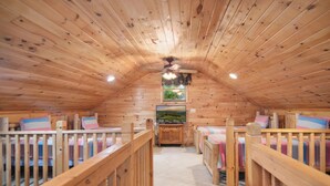 Ein gemütliches Schlafzimmer im Dachgeschoss mit Holzwänden und schrägen Wänden, mit zwei Betten mit Holzgeländern und einem kleinen Fenster mit Blick auf Grünflächen.