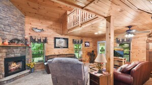 Ein gemütliches Blockhaus-Interieur mit Kamin, Holzwänden, einer komfortablen Sitzecke und einem Balkon mit Aussicht.