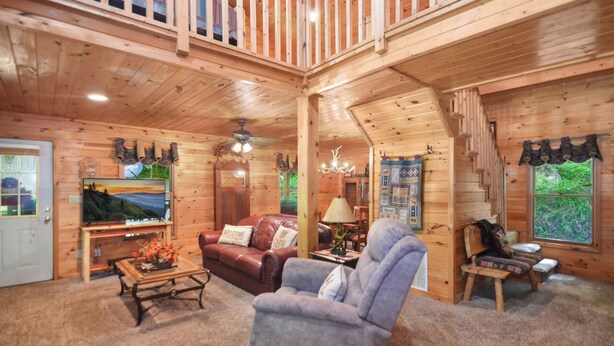 Ein Holzblockhaus-Interieur mit Wohnzimmer, Fernseher, Kamin und einem Balkon.