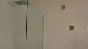 Een badkamer met een douche met glazen wand, witte betegelde wanden en een wit toilet.