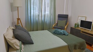 Een netjes ingerichte hotelkamer met een bed, een stoel, een bureau met een computer en een lamp.