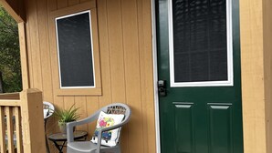 A wooden porch with a green door, two chairs, a small table, and a potted plant. - Cozy little cabin in a small town  (Caney)