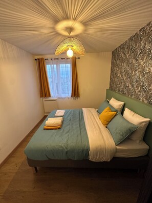 Un dormitorio con cama, cortinas, un papel tapiz estampado y una lámpara en el techo.