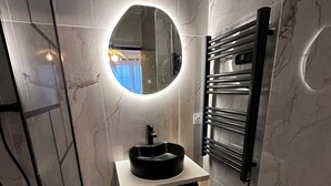 Une salle de bain moderne avec un pare-baignoire en marbre, un miroir rond, un lavabo noir et un porte-serviettes.