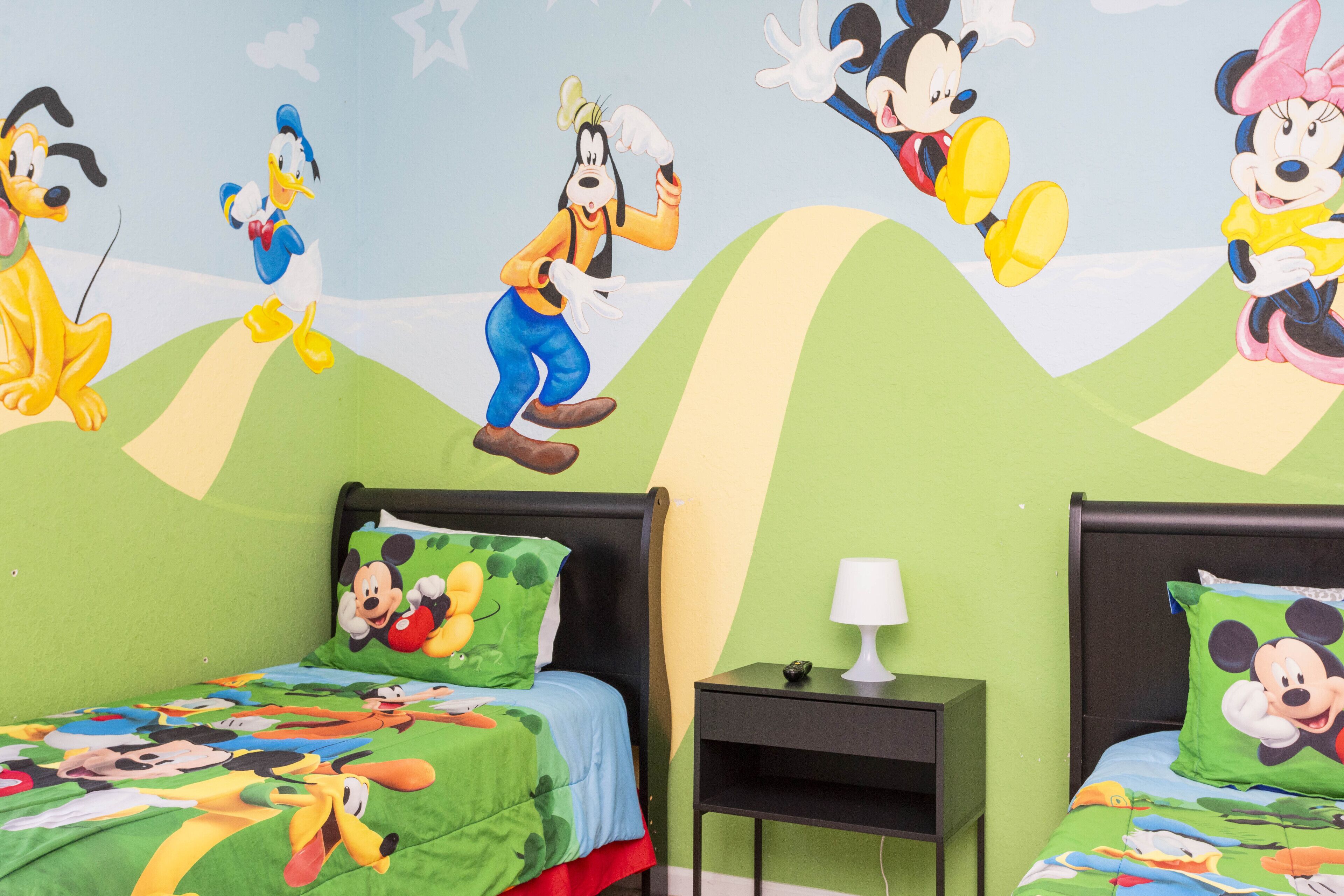 Habitación infantil con dos camas, cada una decorada con diseños de Mickey Mouse y Donald Duck.