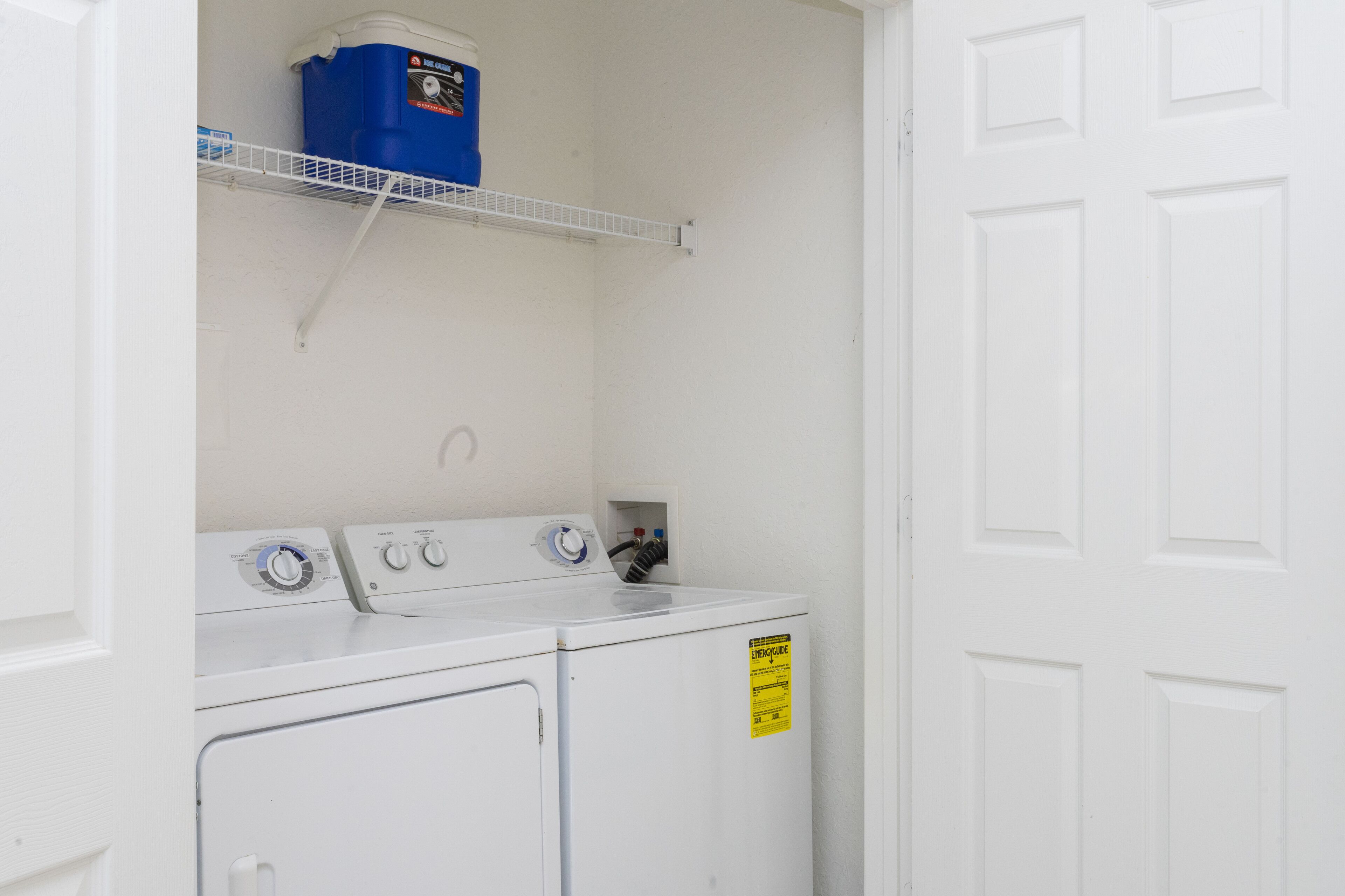 A laundry area with two white washing machines, a blue container on a shelf, and a yellow recycling sign.