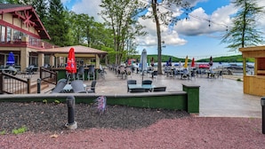 An outdoor patio area with tables and chairs, surrounded by trees and a building with a red exterior.