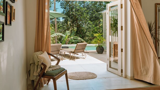 Puerta abierta que da a un patio con piscina, sillas y una mesa.