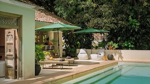 Un área junto a la piscina con sillones, sombrillas y plantas en macetas.