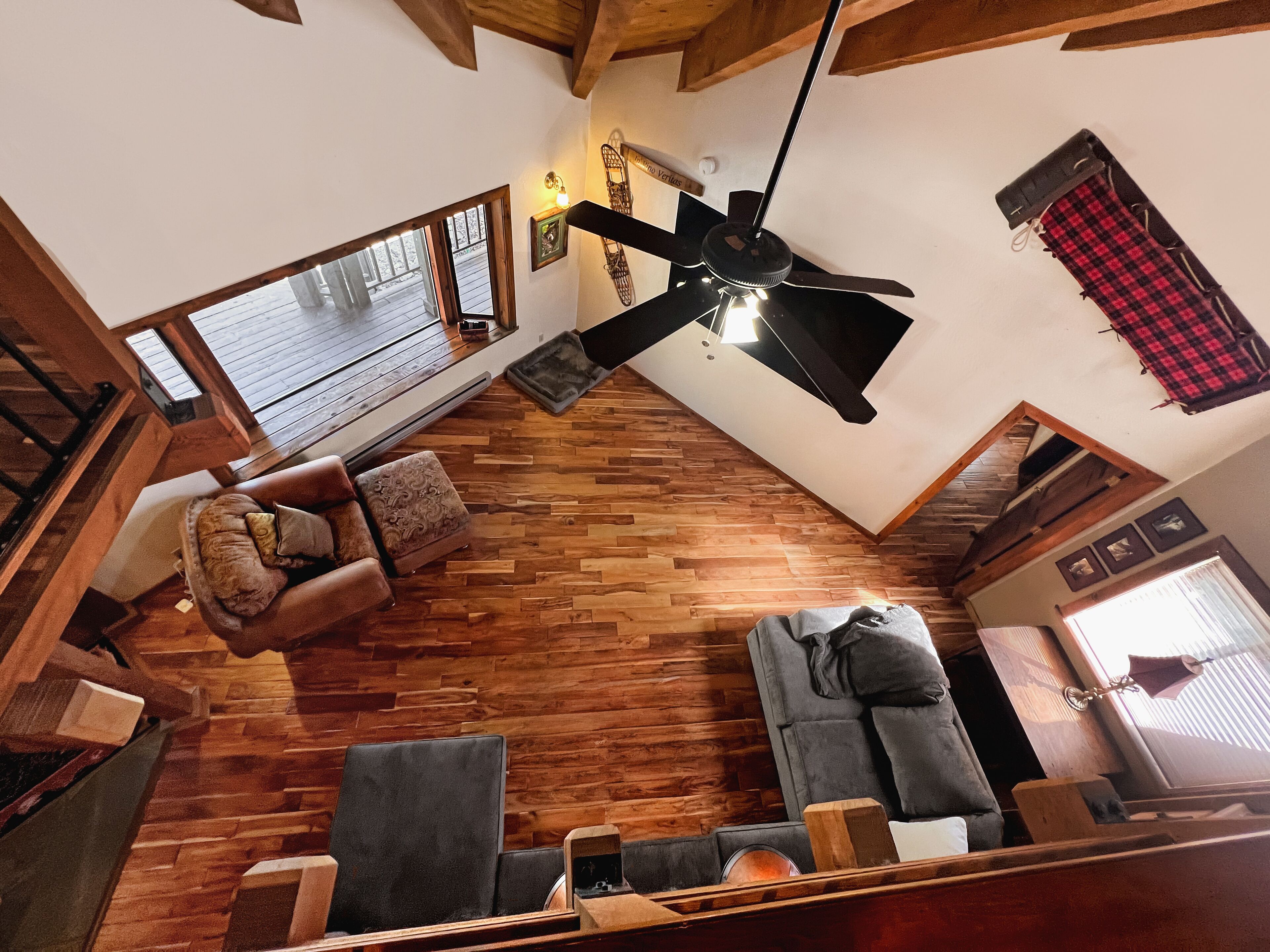 A spacious living area with a high ceiling, wooden flooring, and a ceiling fan. There are two sofas and a coffee table, with a fireplace and a window providing natural light.